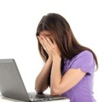 Woman covering face in front of a laptop computer